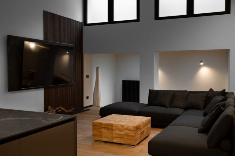 Zona TV con boiserie in legno, luci LED e divano scuro