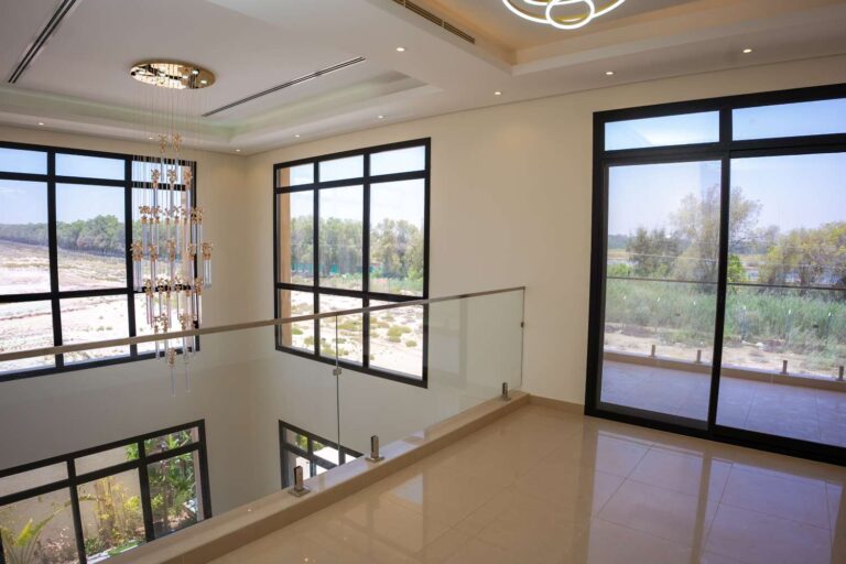 Vista sulla doppia altezza vetrata con parapetto in vetro e illuminazione a sospensione in una villa moderna a Dubai