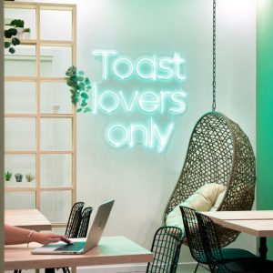 angolo con altalena sospesa, scritta led “Toast lovers only” e tavolini in legno chiaro