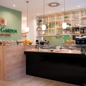 bancone bar moderno in legno chiaro con esposizione dolci e parete verde con logo Toast Garden