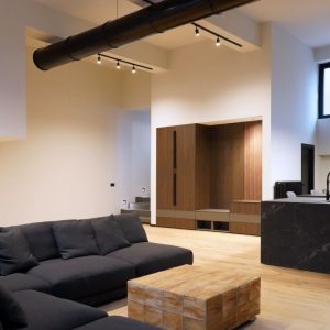Ampio open space con divano nero, cucina con isola e arredi in legno
