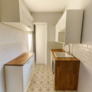 lavanderia compatta con pensili bianchi, top in legno e pavimento decorato