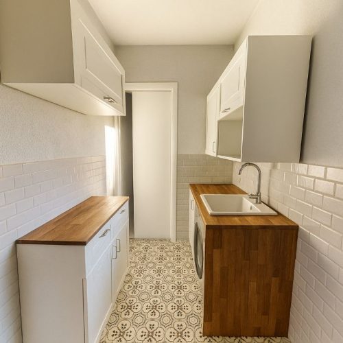 lavanderia compatta con pensili bianchi, top in legno e pavimento decorato