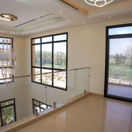 Vista sulla doppia altezza vetrata con parapetto in vetro e illuminazione a sospensione in una villa moderna a Dubai