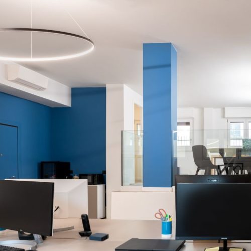 open space ufficio con postazioni operative in primo piano e zona riunioni su soppalco in vetro